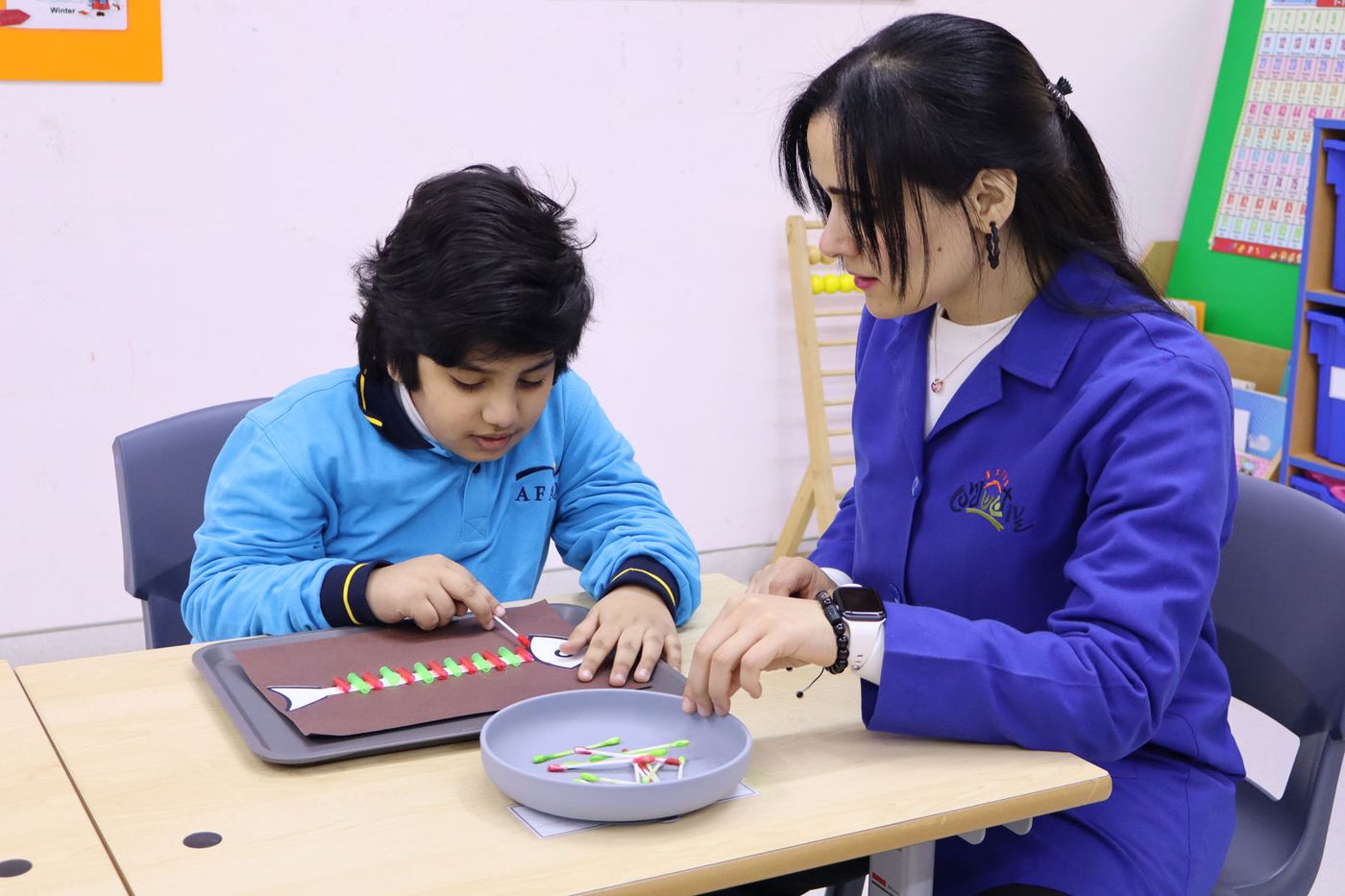 A CESK student threading small pieces in a fine-motor activity with a teacher