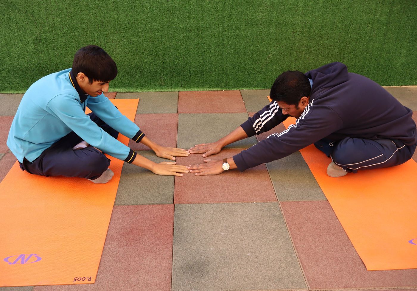 Two CESK students doing stretching exercises together on outdoor mats