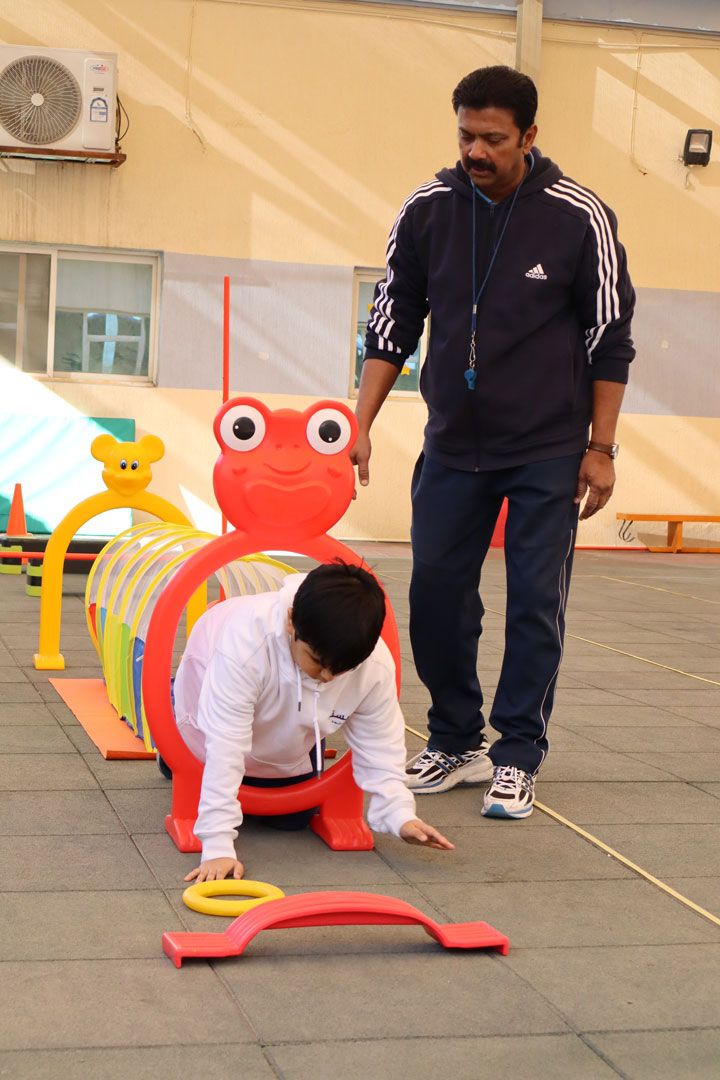 A CESK student crawling through a play tunnel while a staff member watches